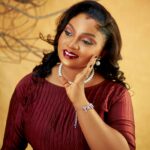 Portrait of a smiling woman in a burgundy dress with elegant jewelry against a neutral background.