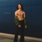 Shirtless male model posing in urban environment with sleek style.