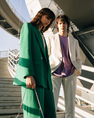 Stylish man and woman posing on a staircase in urban setting, wearing vibrant outfits.